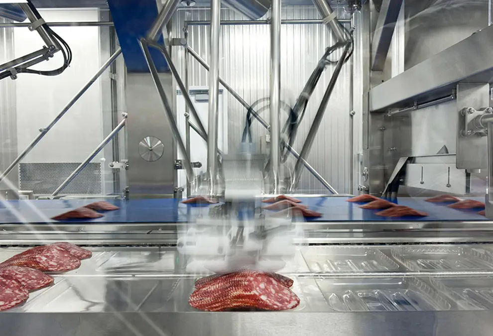 A factory machine processes sliced meat.